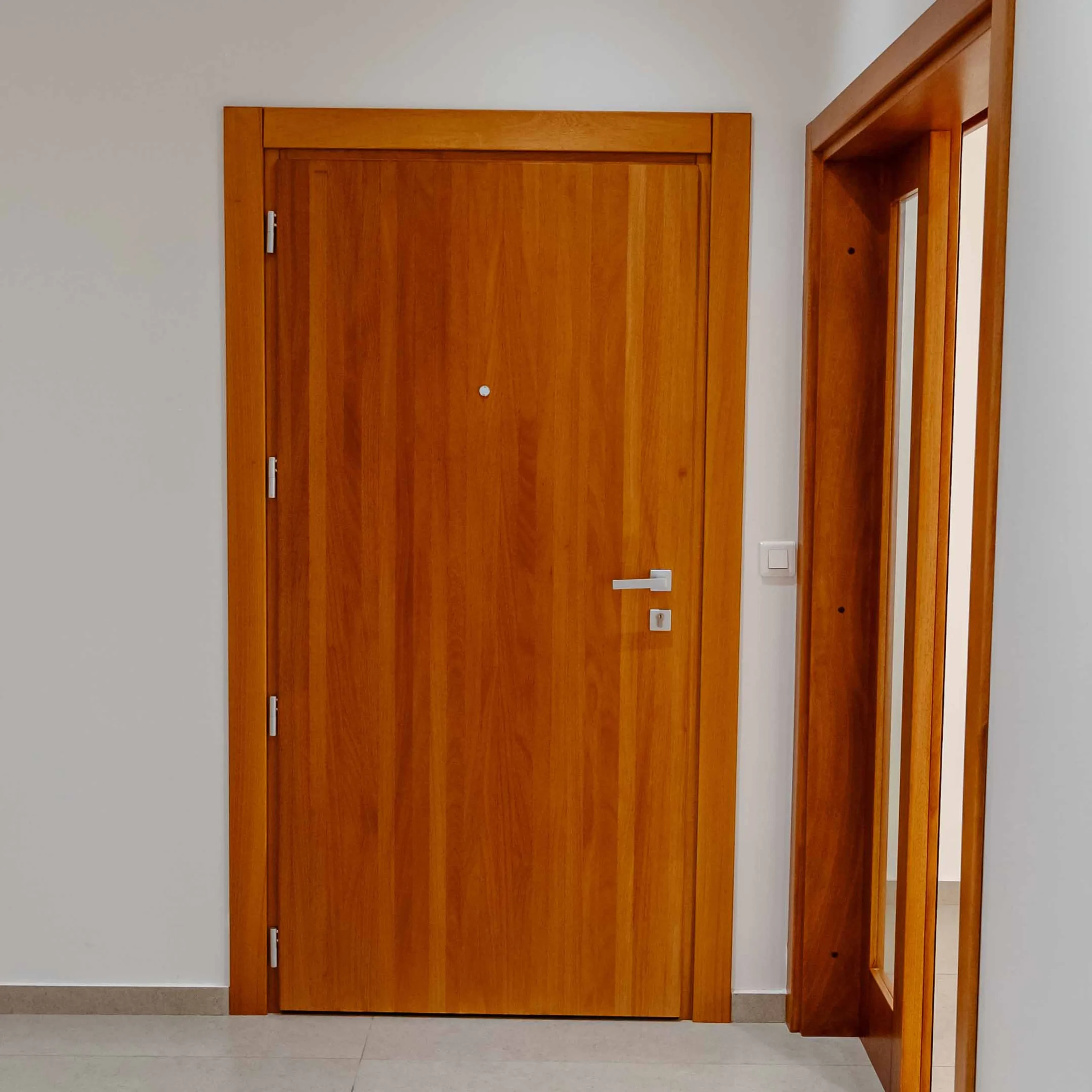 Projetti — Porte intérieure en bois massif design moderne Projetti — Porte intérieure en bois massif de couleur chêne clair, avec deux poignées verticales et une serrure à bouton, située dans un couloir blanc