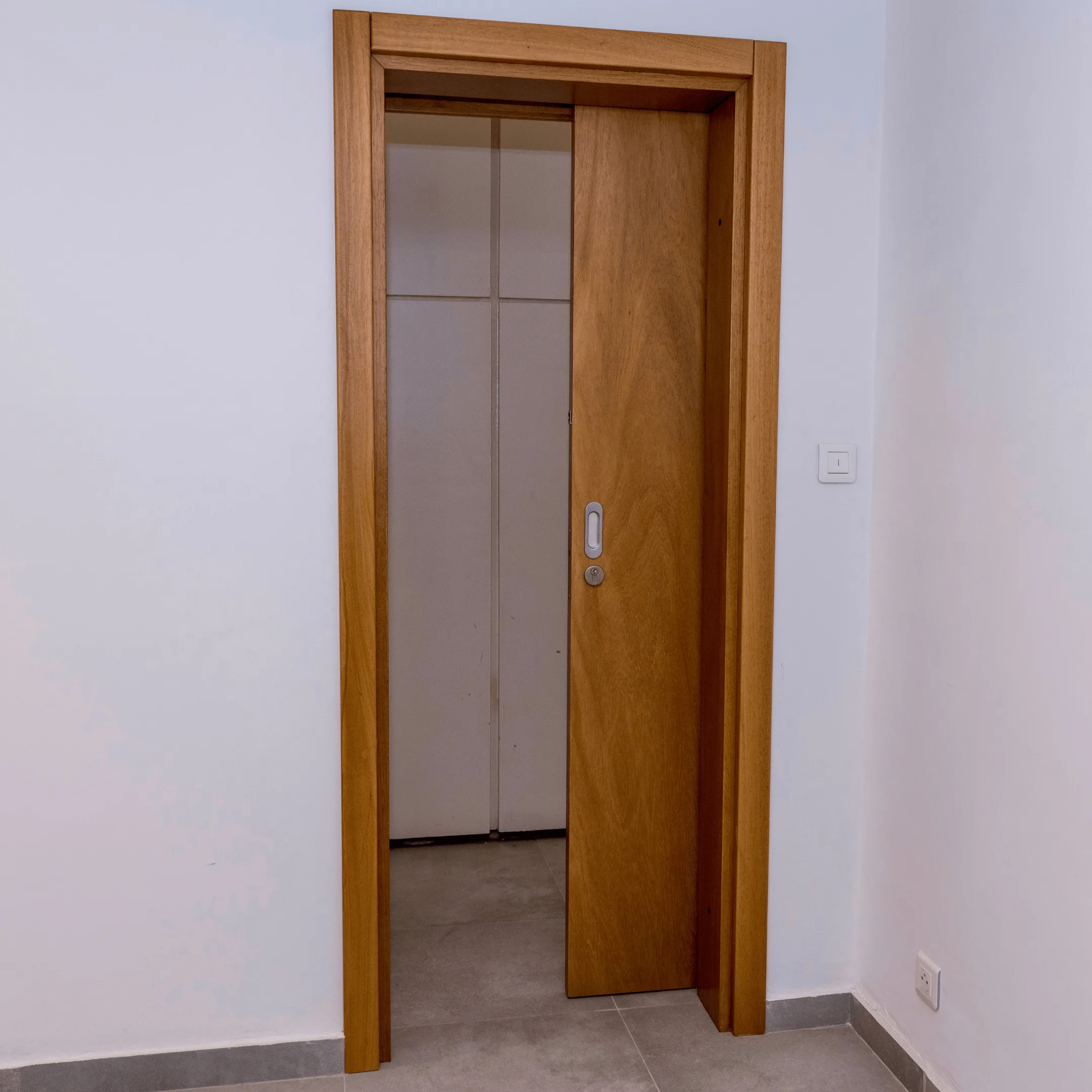 Projetti — Portes intérieures en bois design Projetti — Deux portes intérieures en bois clair, légèrement entrouvertes, révélant un couloir ou une pièce blanche avec un sol carrelé clair et un in